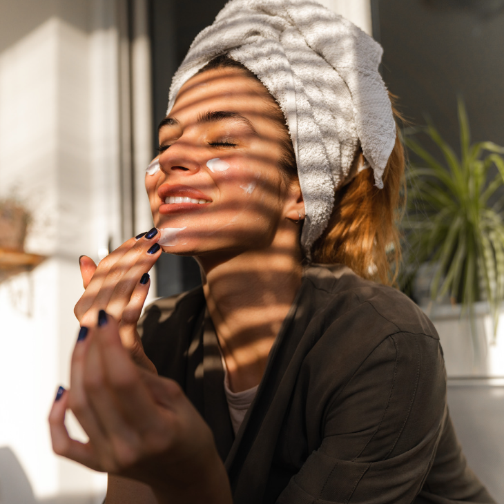 woman applying skincare products while facing an open window