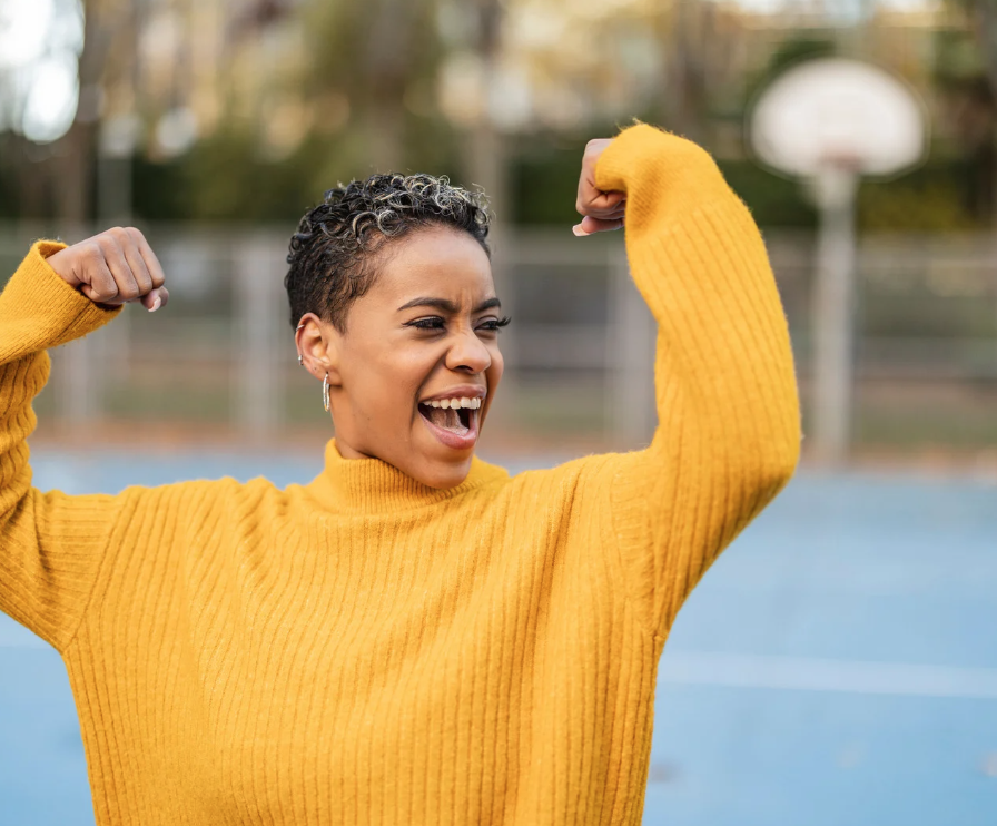 an empowered woman wearing a yellow sweater and arms up in a flexing position