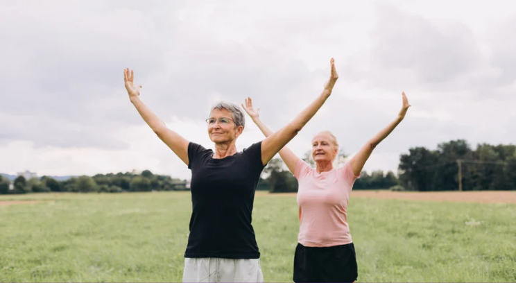 exercise: 2 women in an open field stretching their arms up