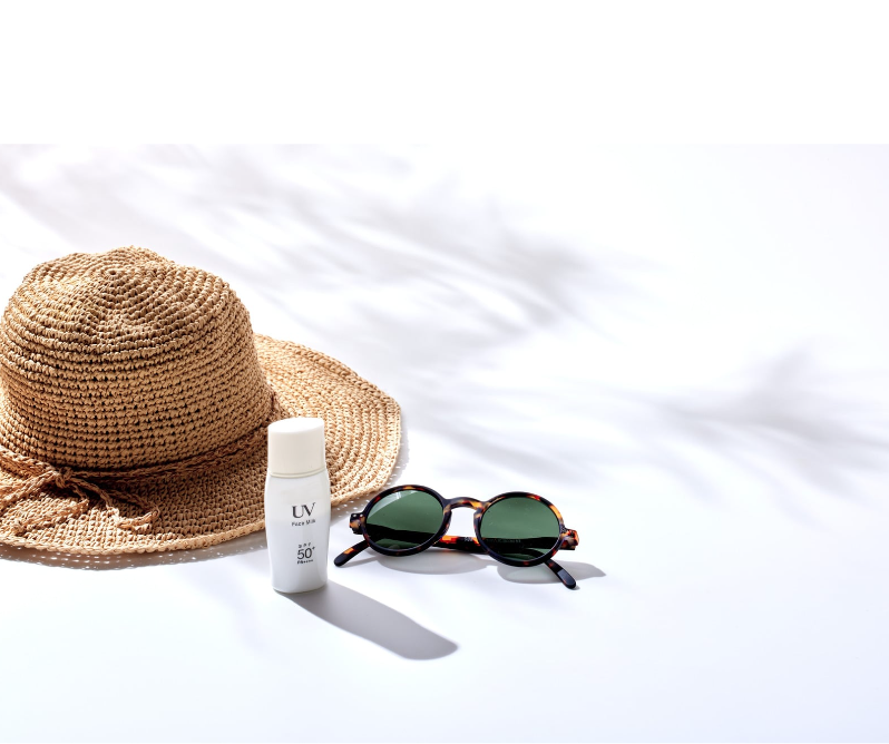 Straw sun hat, sunscreen SPF 50, and sunglasses arranged for summer skincare and sun protection.