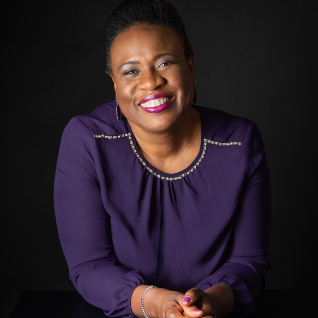 Evelyn Abernathy smiling in a purple blouse against a dark background